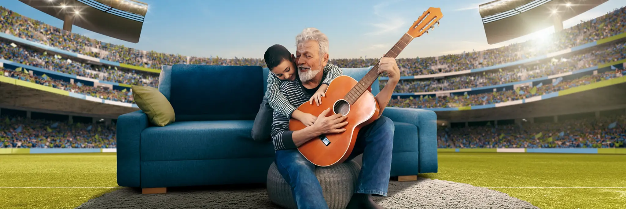 Man with a guitar smiling with a boy on a blue chair in front of a blue couch in a football stadium